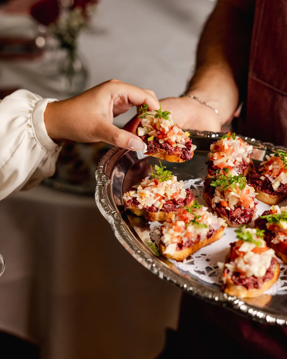 Server passing crostini on a silver tray as a guest holds champagne